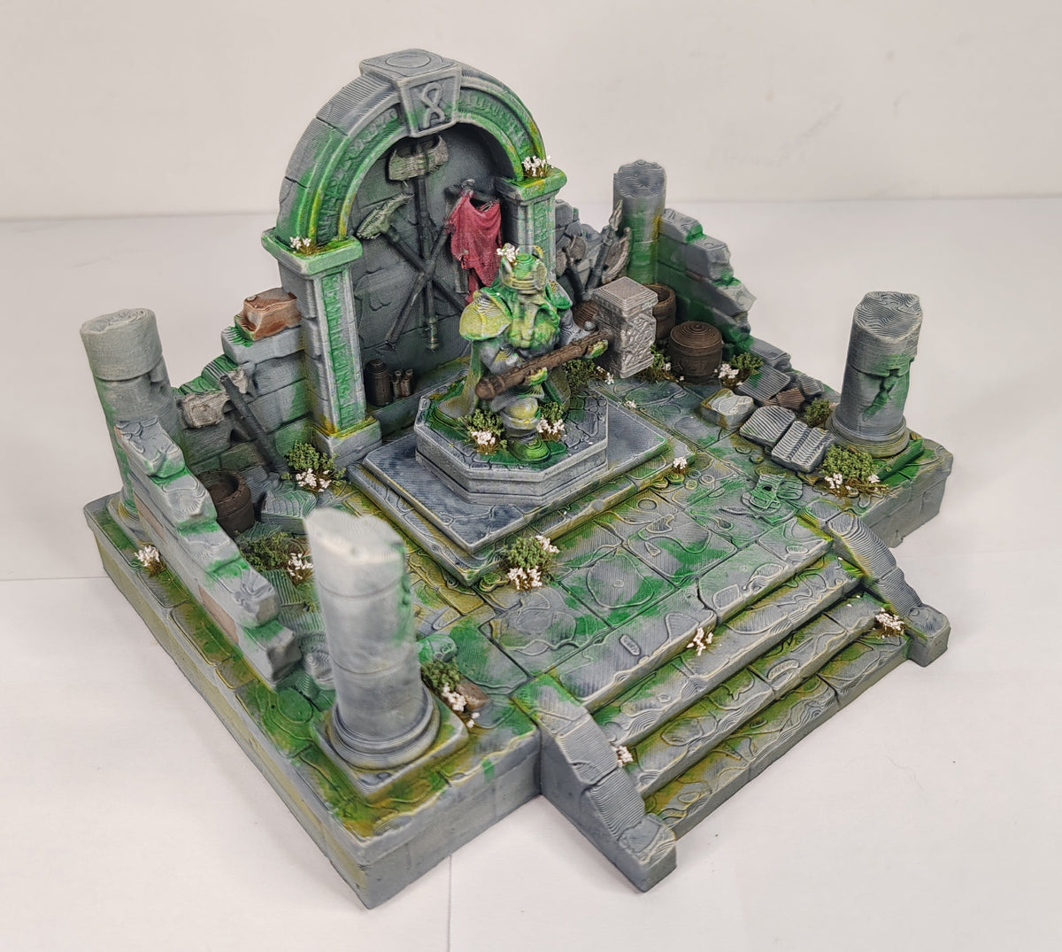 A painted miniature tabletop terrain piece depicting a stone staircase leading up to a ruined archway with a green-skinned warrior statue in the center, set against a plain white background.