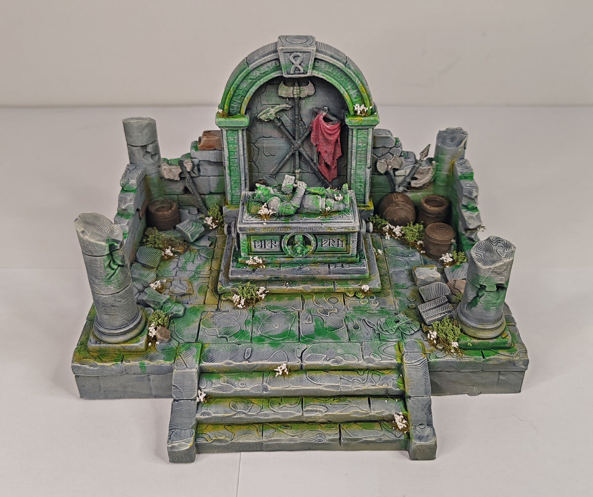 A miniature tabletop gaming diorama set depicting a ruined stone temple or altar with steps, mossy green details, gray stone textures, and a small red-robed figure standing in the center.