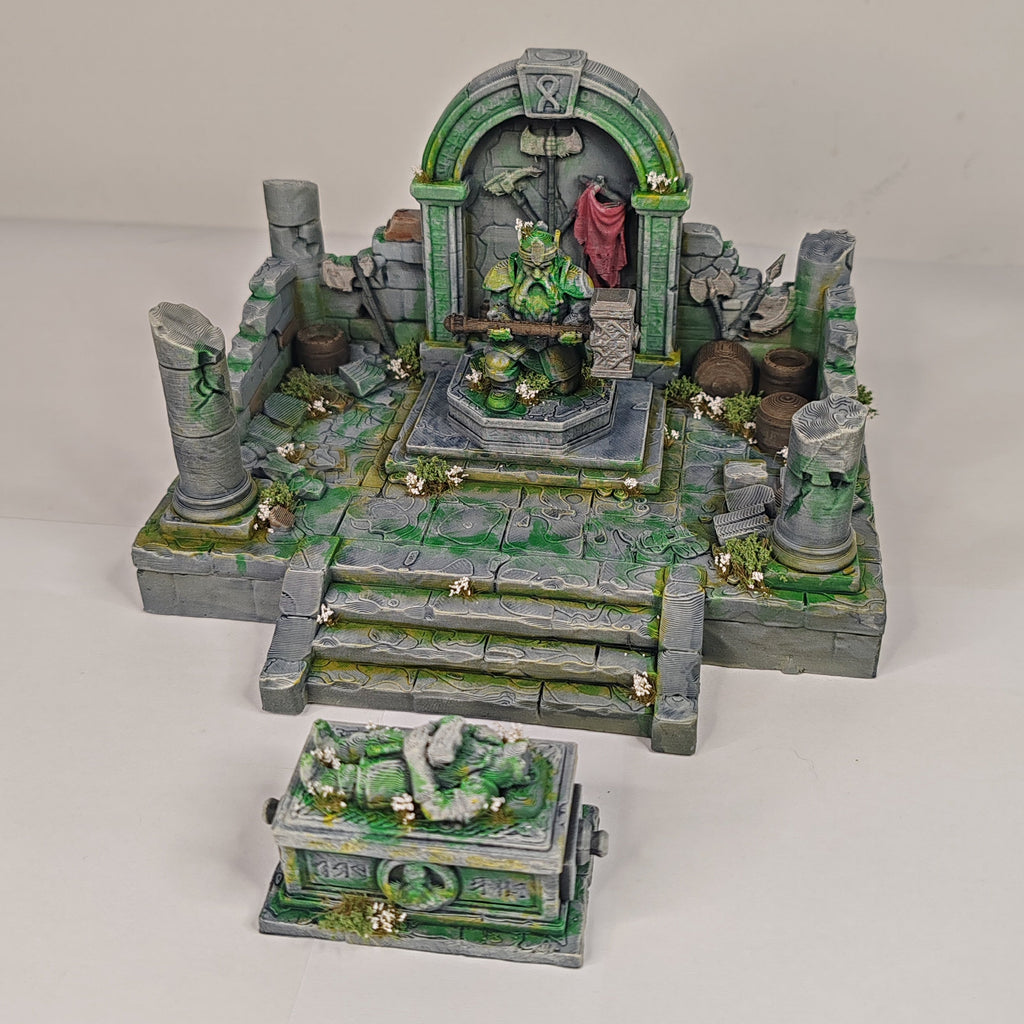 A miniature fantasy ruins set with a stone archway, steps, pillars, and a small chest or crate in front, photographed on a plain light background.