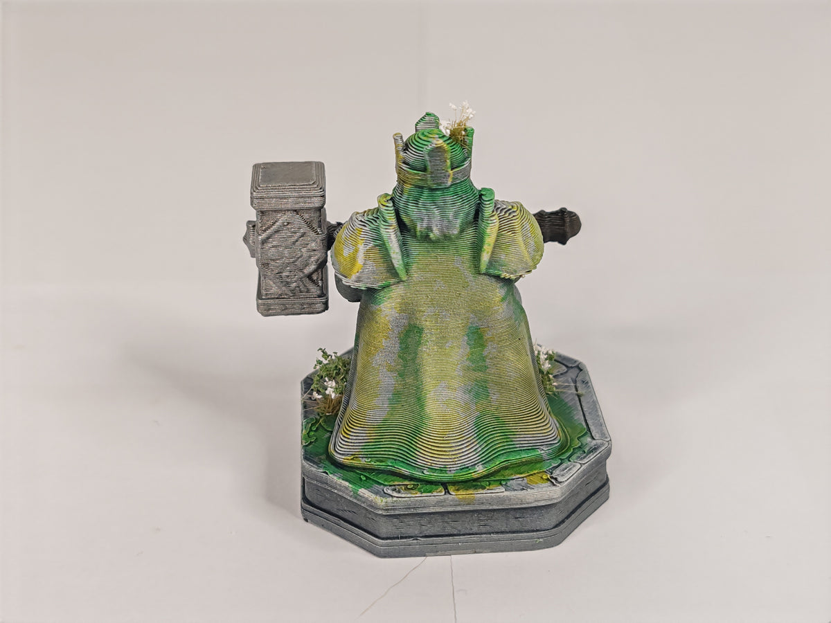 A 3D-printed miniature figurine of a crowned queen or king in a green robe holding a gray mace, standing on a gray base against a white studio background.