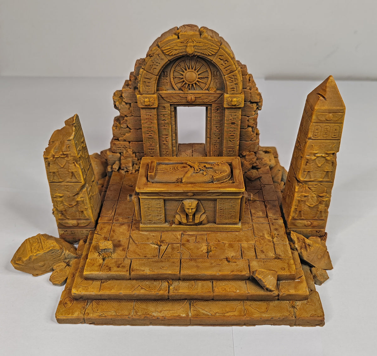 A small carved wooden miniature temple or altar set with an arched doorway, central table, pedestal, and two tall obelisks, photographed against a plain light background.