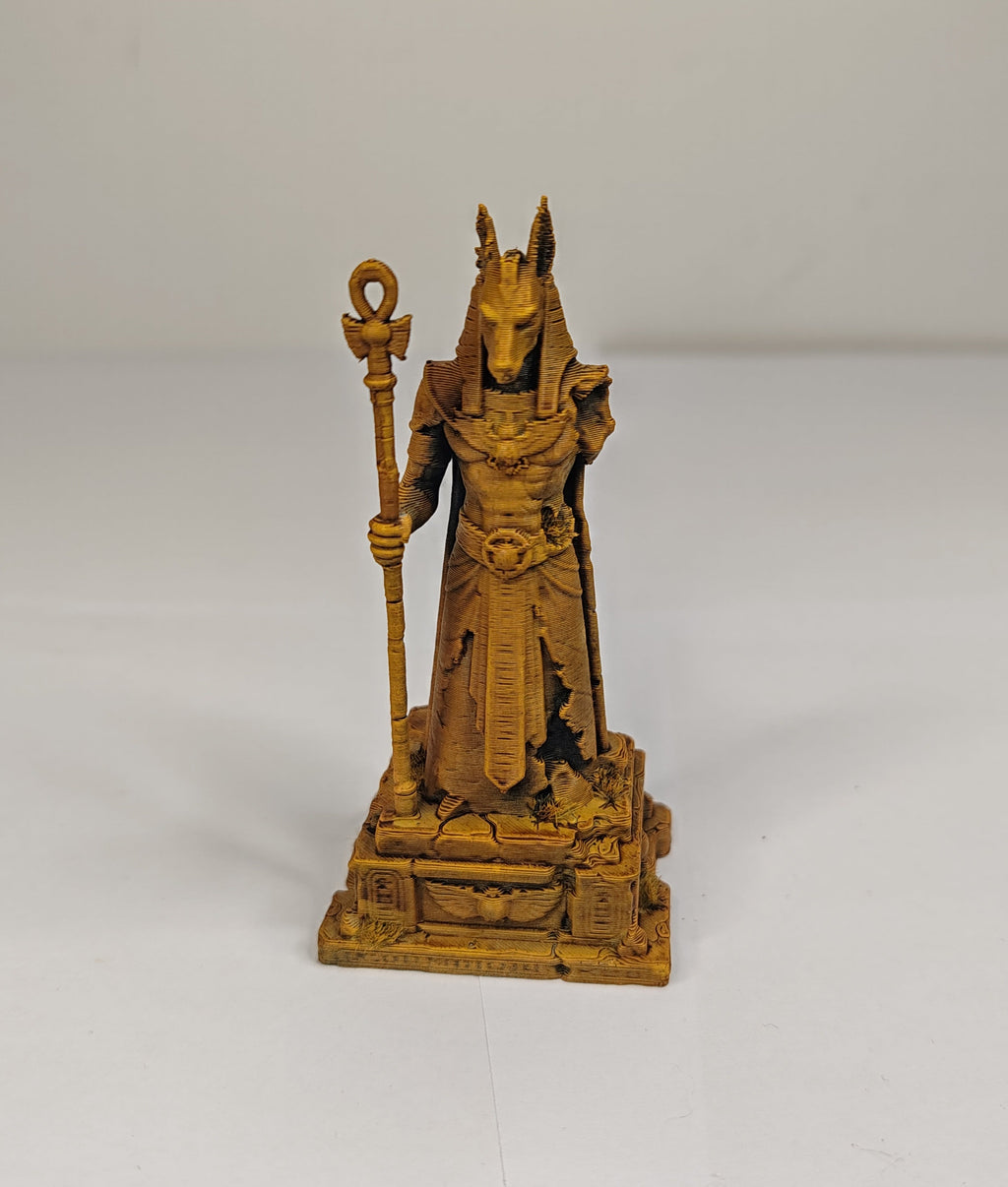 A small golden-brown fantasy figurine of a horned deity or king holding a staff, standing on a detailed base against a plain light background.